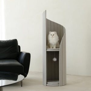 Cat sitting on top platform of Time Travel Tower Cat Tree in Light Grey, with minimalist design next to modern black sofa.