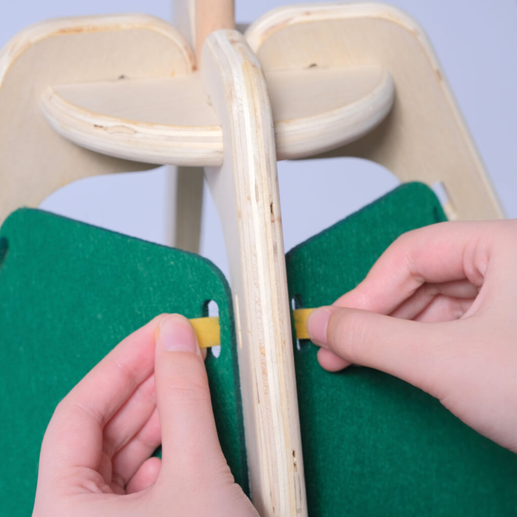  Close-up of hands adjusting the yellow connectors on the wooden frame of the green felt pet tent.