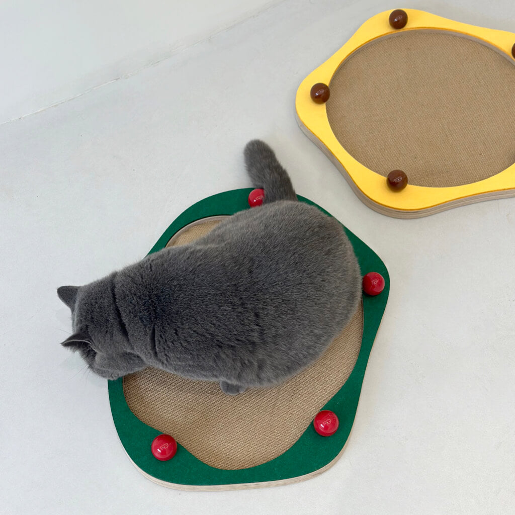Cat playing on green Sisal Cat Scratcher Panel with red ceramic decorative balls next to a yellow version.