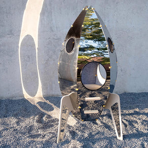 Rocket-shaped mirrored cat tower in a contemporary outdoor setting.
