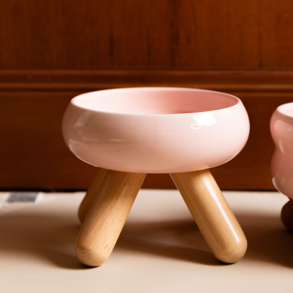 Side view of cherry pink ceramic pet food bowls with sturdy wooden legs.
