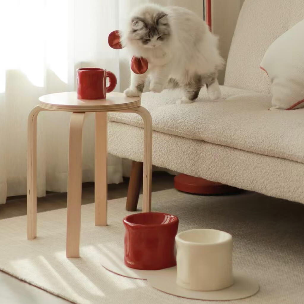 Pinch Ceramic Mug & Elevated Pet Bowl Set – Bordeaux Red with Cat – A playful cat with a red bowtie interacts with the Pinch ceramic mug and elevated pet bowl set in Bordeaux red, placed on a wooden table.