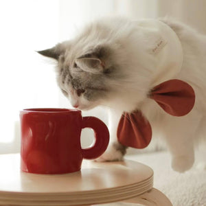 Cat Sniffing Pinch Ceramic Mug – Bordeaux Red – A close-up of a cat curiously sniffing the Pinch ceramic mug in Bordeaux red, set on a light wooden table.
