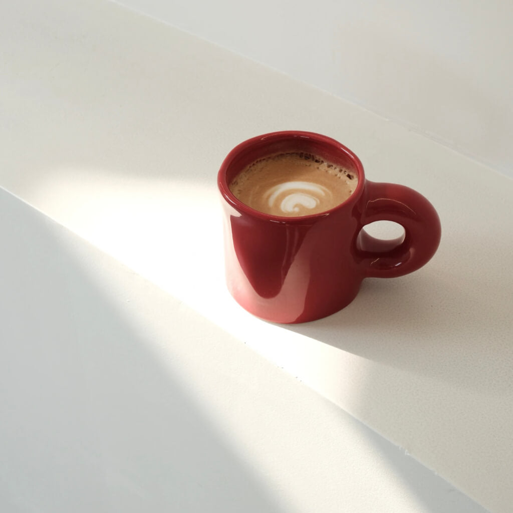 Pinch Ceramic Mug in Bordeaux Red, filled with a latte and beautifully lit by natural sunlight. A perfect match for the Meoof Elevated Pet Bowl for coordinated pet and human dining.