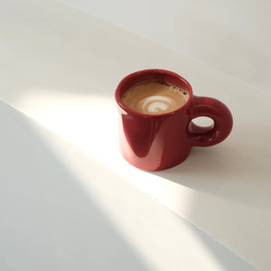 Pinch Ceramic Mug in Bordeaux Red, filled with a latte and beautifully lit by natural sunlight. A perfect match for the Meoof Elevated Pet Bowl for coordinated pet and human dining.
