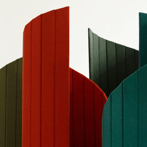 Close-up image of the top part of two Time Travel Cat Towers in different colors—one in red and one in dark green. The focus is on the sleek, curved design and textured fabric exterior, demonstrating the variety of color options available for this modern cat furniture piece.