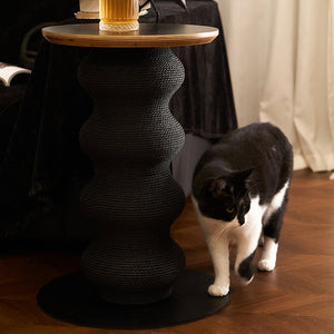 Black and white cat walking beside Coral Cat Scratcher used as a stylish end table with drink on top.