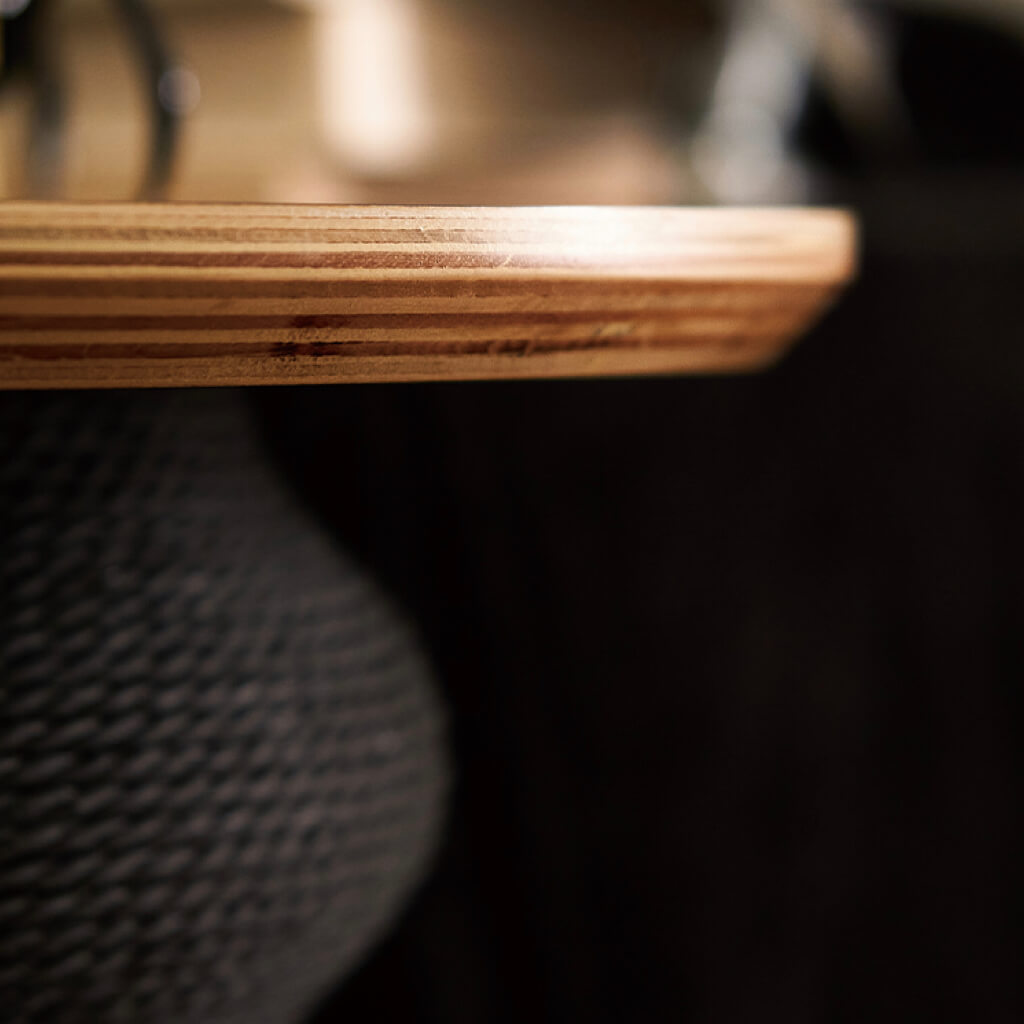 Close-up of natural wood tabletop edge with rope-textured black scratching module in background.