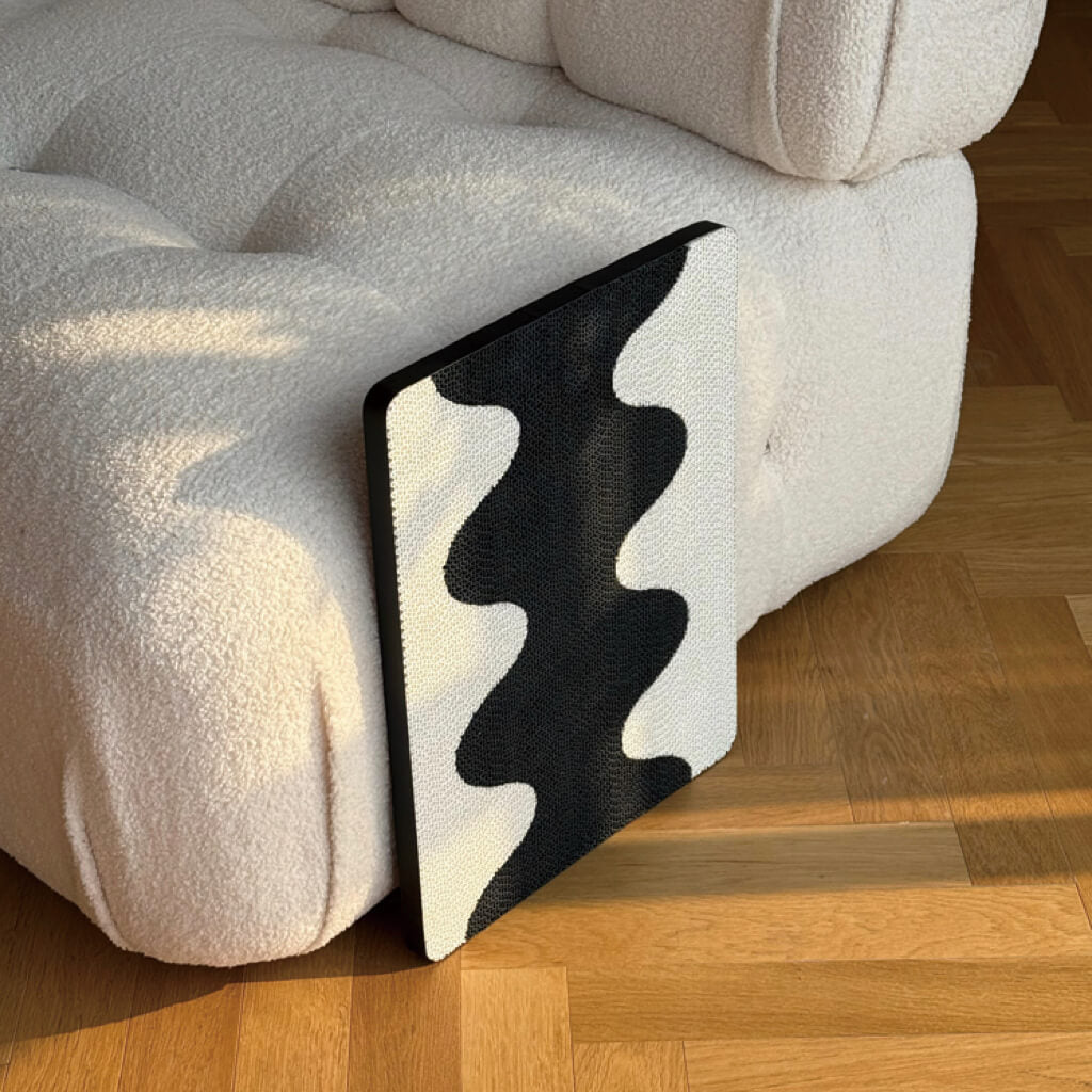 Coral Cat Scratching Pad with sleek black-and-white wave pattern leaning against cream sofa