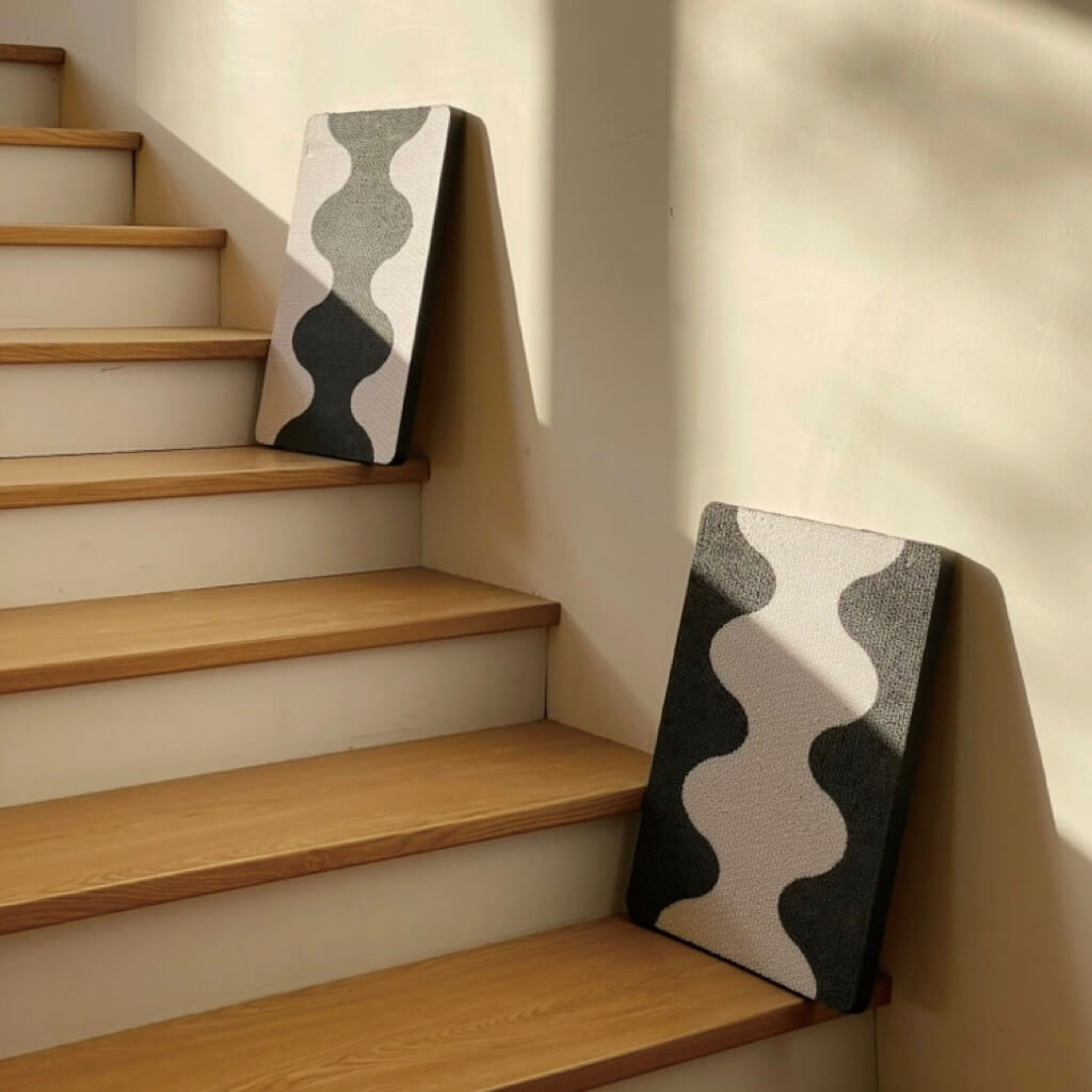 Two Coral Cat Scratching Pads leaning on stairs with minimalist black-and-white wave design