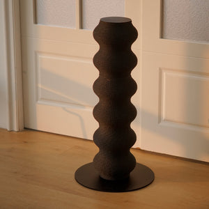 Black wavy cat scratching post in minimalist modern room, standing on light wooden floor with soft natural light.