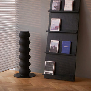 Modern black wavy cat scratcher next to magazine shelf and window blinds, styled in contemporary home corner.