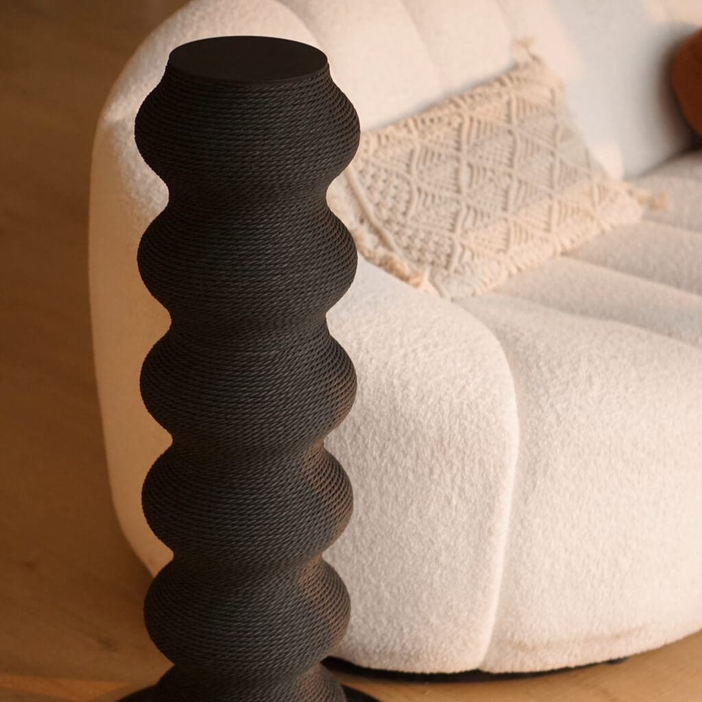 Close-up of sculptural black cat scratching post beside cream boucle sofa in cozy minimalist living space.