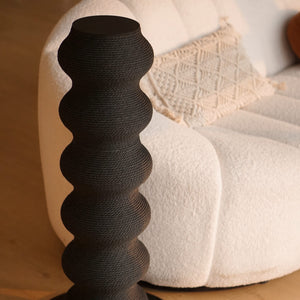 Close-up of sculptural black cat scratching post beside cream boucle sofa in cozy minimalist living space.