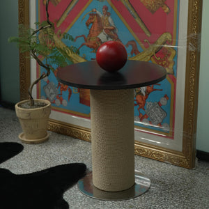 Design cat scratcher and side table with black round top, natural sisal column, and polished metal base; styled beside framed artwork.