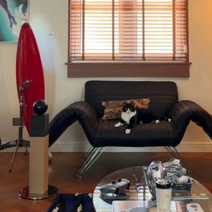 Matchstick-style cat scratcher with black orb top beside contemporary sofa; durable sisal and stable base for modern interiors.
