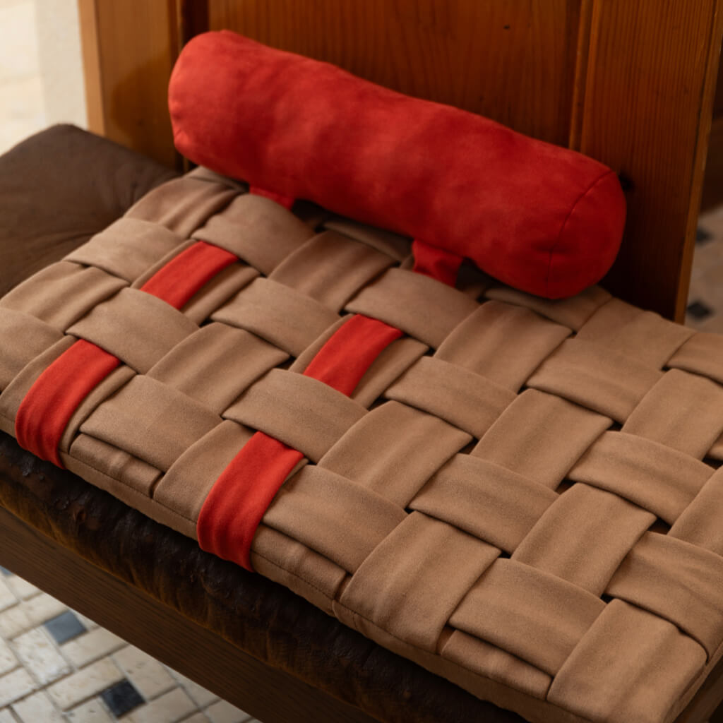 Handwoven Design Pet Mat - Orange and Brown on a chair, showcasing the woven surface and cozy pillow.