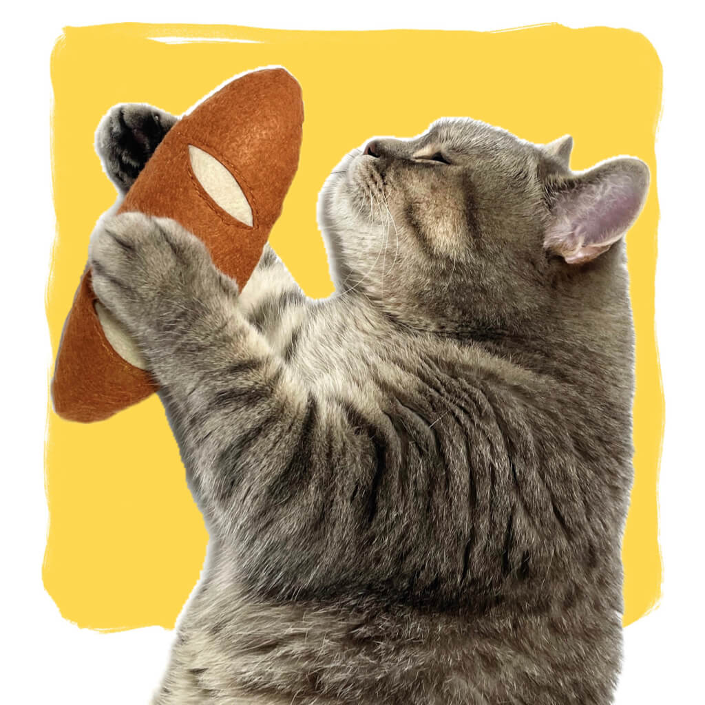 Gray cat holding a wool felt baguette cat toy from PoketPet Bakery.