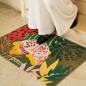 Person standing on decorative jungle-style litter mat with colorful cat design – home entryway view.