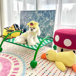 Small white dog in a green checkerboard patterned Memphis Maze hammock in a playful setting.