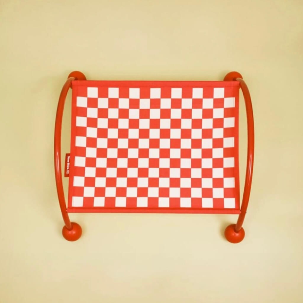 Stylish red cat hammock featuring a vibrant checkerboard pattern on a plain cream background.