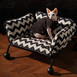 A Sphynx cat lounging on a Memphis-style elevated pet bed, featuring a bold zigzag design and ergonomic support.