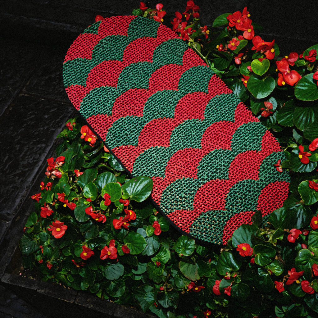 Red and green Koi Fish-inspired cat scratcher surrounded by vibrant garden flowers.