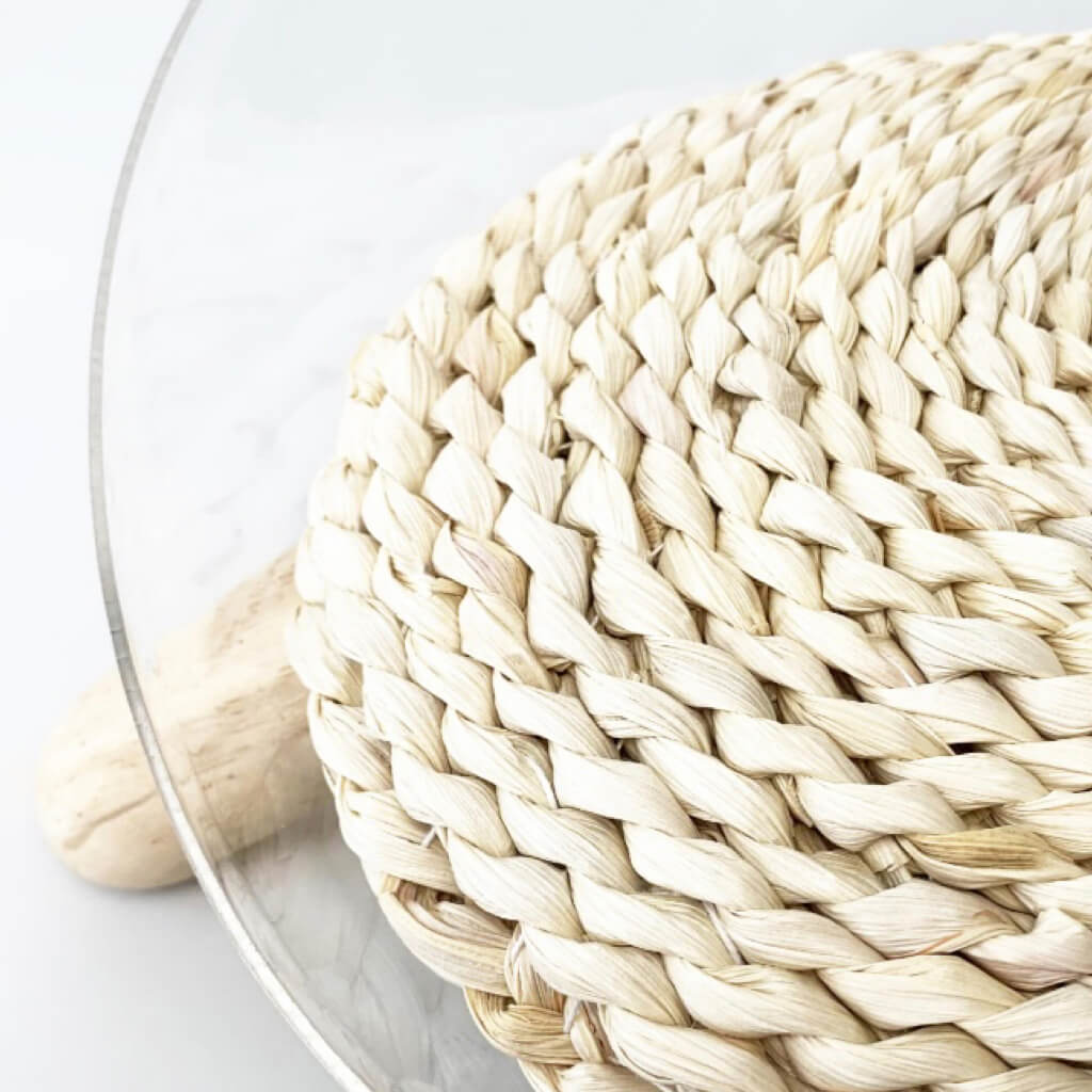 Close-up of braided corn husk cushion inside clear cat bowl bed with modern wooden legs