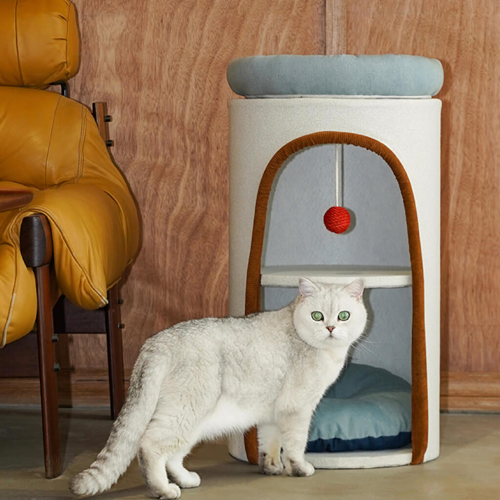 Modern cat tower with blue bed and red toy ball, styled in cozy home setting with a cat sitting in front.