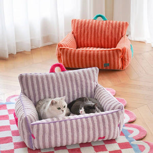 Two cats resting in purple striped plush cat bed, orange bed in background – sofa-style pet lounger.
