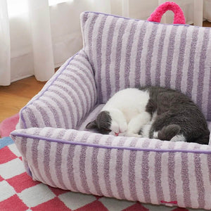 Cat sleeping curled up in purple striped plush cat bed with soft cushioned backrest.