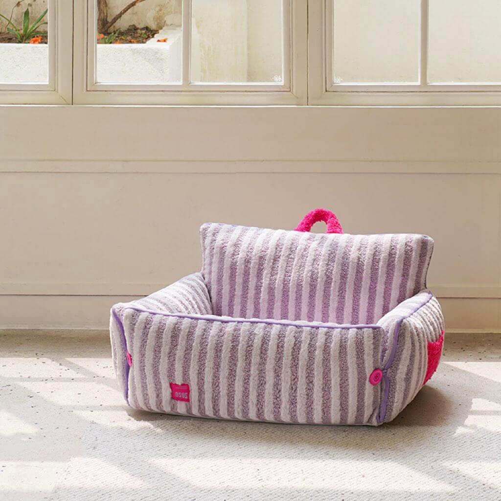 Empty purple striped plush cat bed with backrest in sunlit room.
