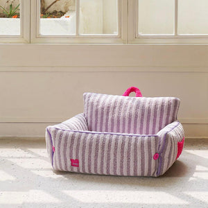 Empty purple striped plush cat bed with backrest in sunlit room.