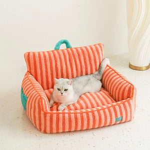 Cat lying in orange striped plush cat bed with backrest and green handle.