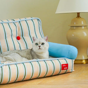 Cat sitting comfortably on ZEZE striped pet sofa next to a beige table lamp