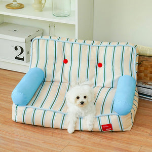 Small white poodle relaxing on spacious striped pet sofa with plush side bolsters