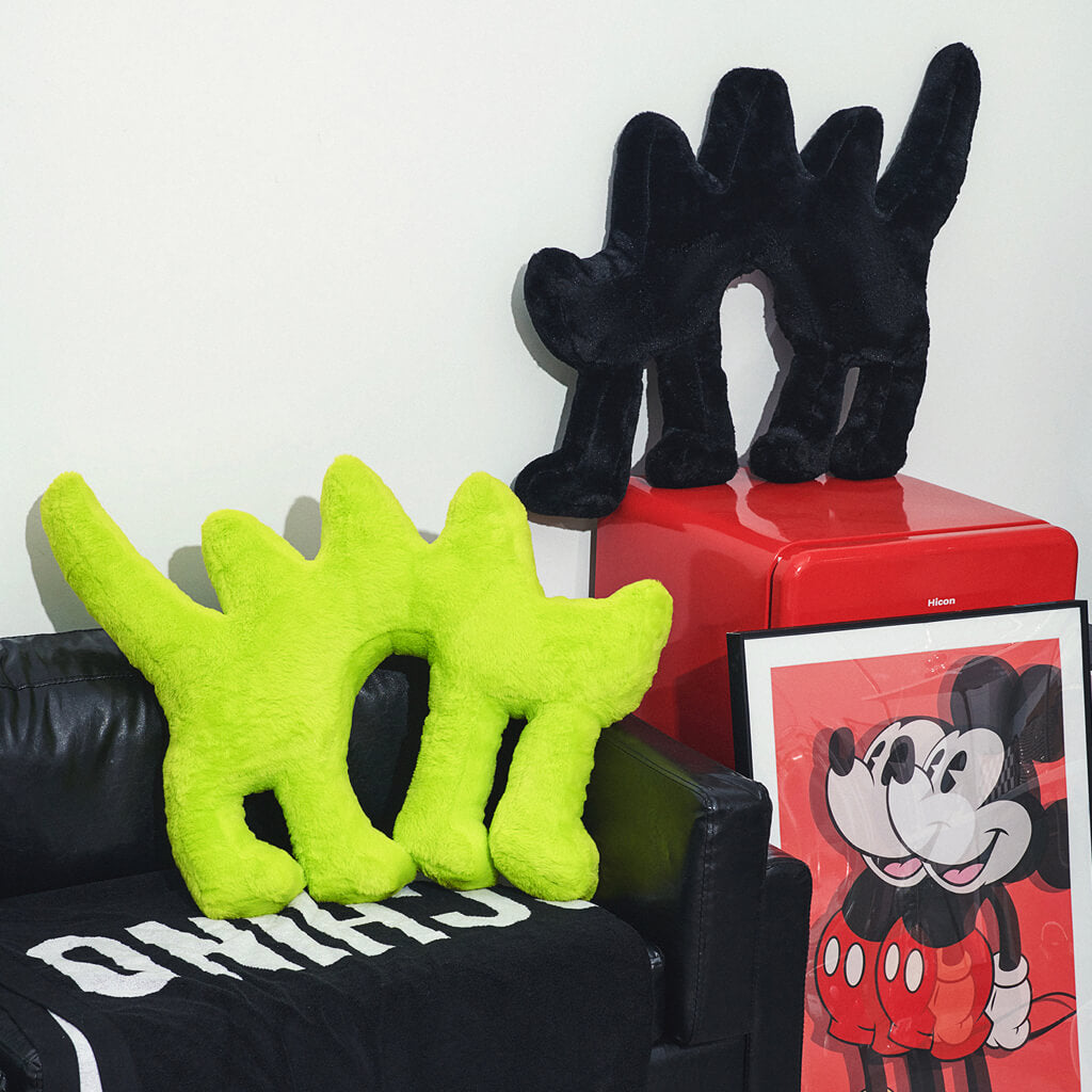 Fluo Green Boom Boom Cat Cushion with a black Boom Boom Cat Cushion on a red side table.