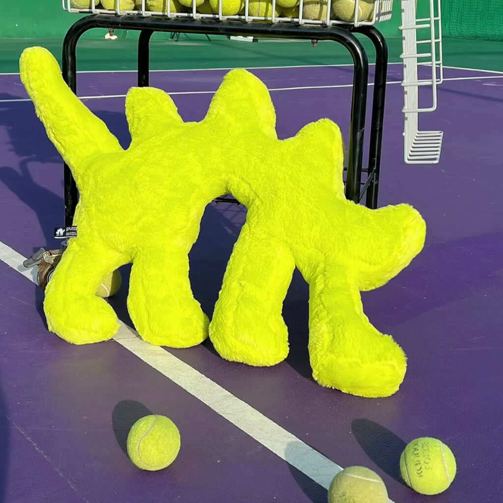 Fluo Green Boom Boom Cat Cushion on a tennis court surrounded by tennis balls.