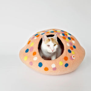 cat lounging in a peach-pink polka dot felt cat bed, showcasing the cave's entrance.
