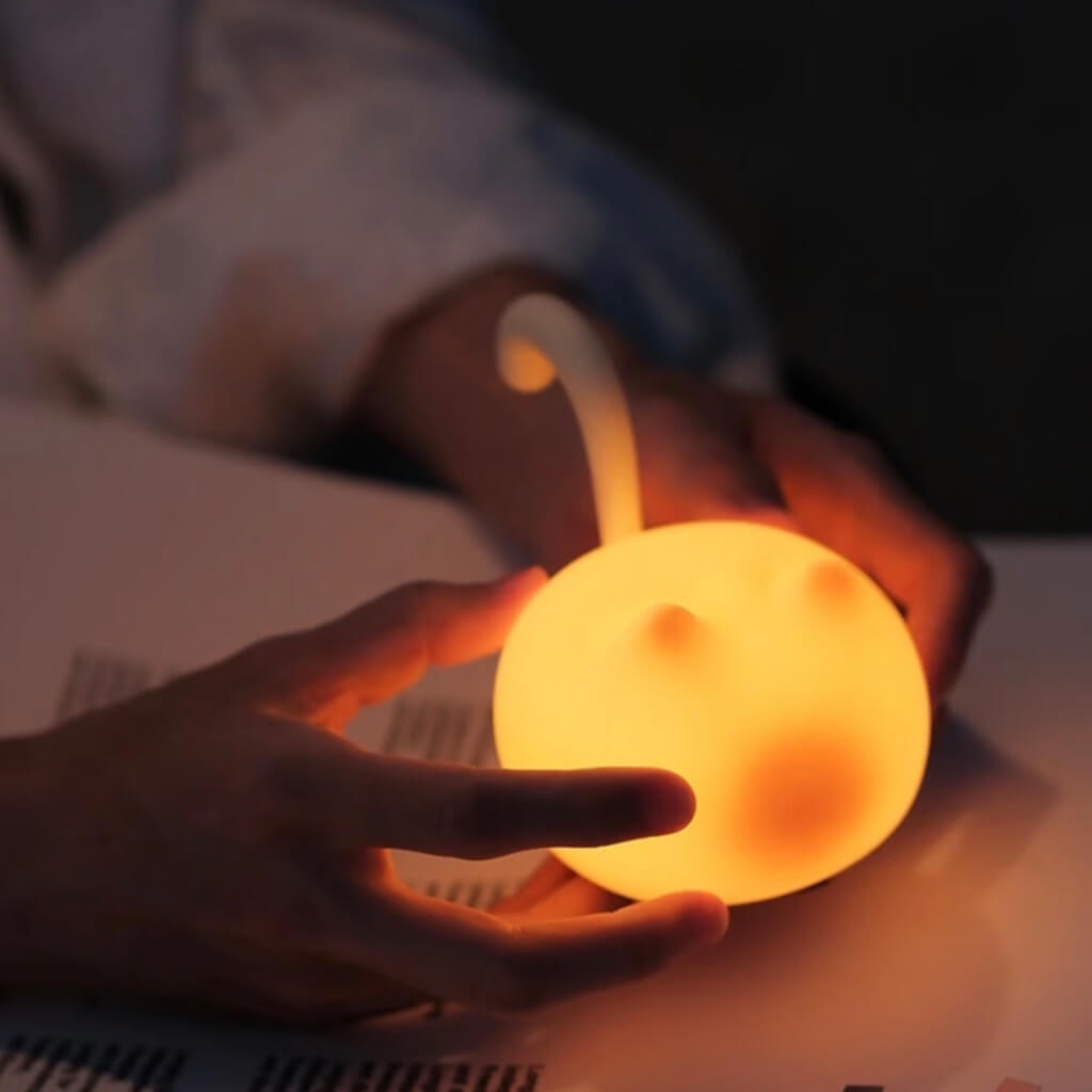 Hand holding the cat-shaped tap night light — squishy silicone shell, tap to dim, portable design.