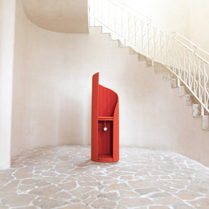 The red Time Travel Cat Tower standing alone in a spacious, neutral-toned room with stone-tiled flooring. The tower’s clean lines and spiral design make it a bold centerpiece against the minimalist backdrop. The dangling pom-pom toy is visible under the top platform.