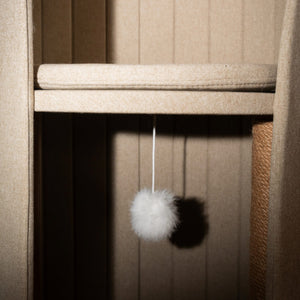 Close-up of the dangling pompom toy inside the beige Time Travel Cat Tower, offering entertainment for playful cats.