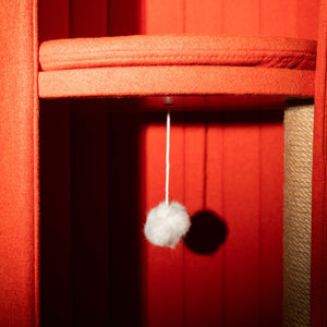 Close-up of the interior of the red Time Travel Cat Tower, showing the soft padded platform and a dangling fluffy white pom-pom toy. The image highlights the cat-friendly features, designed for comfort and interactive play.
