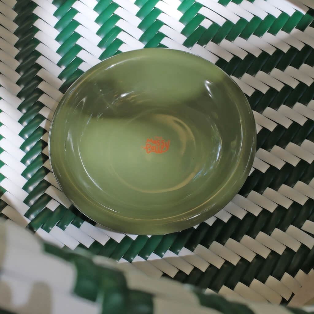 Forest green Messy Paws shallow ceramic cat dish in a green-white woven basket—sleek, whisker-friendly bowl for cats and small dogs.