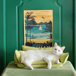 White cat stretched out on the Cozy Pet Sofa Bed - Piped #32 Summer Maple + #31 Jun Green, set against a vibrant Aloha-themed backdrop.