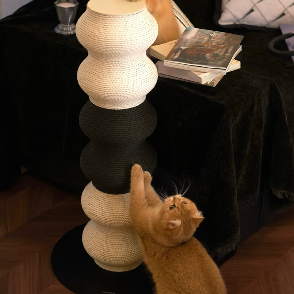 Ginger cat scratching the Coral Cat Scratcher near a side table — wavy black & white post for full-body stretch.