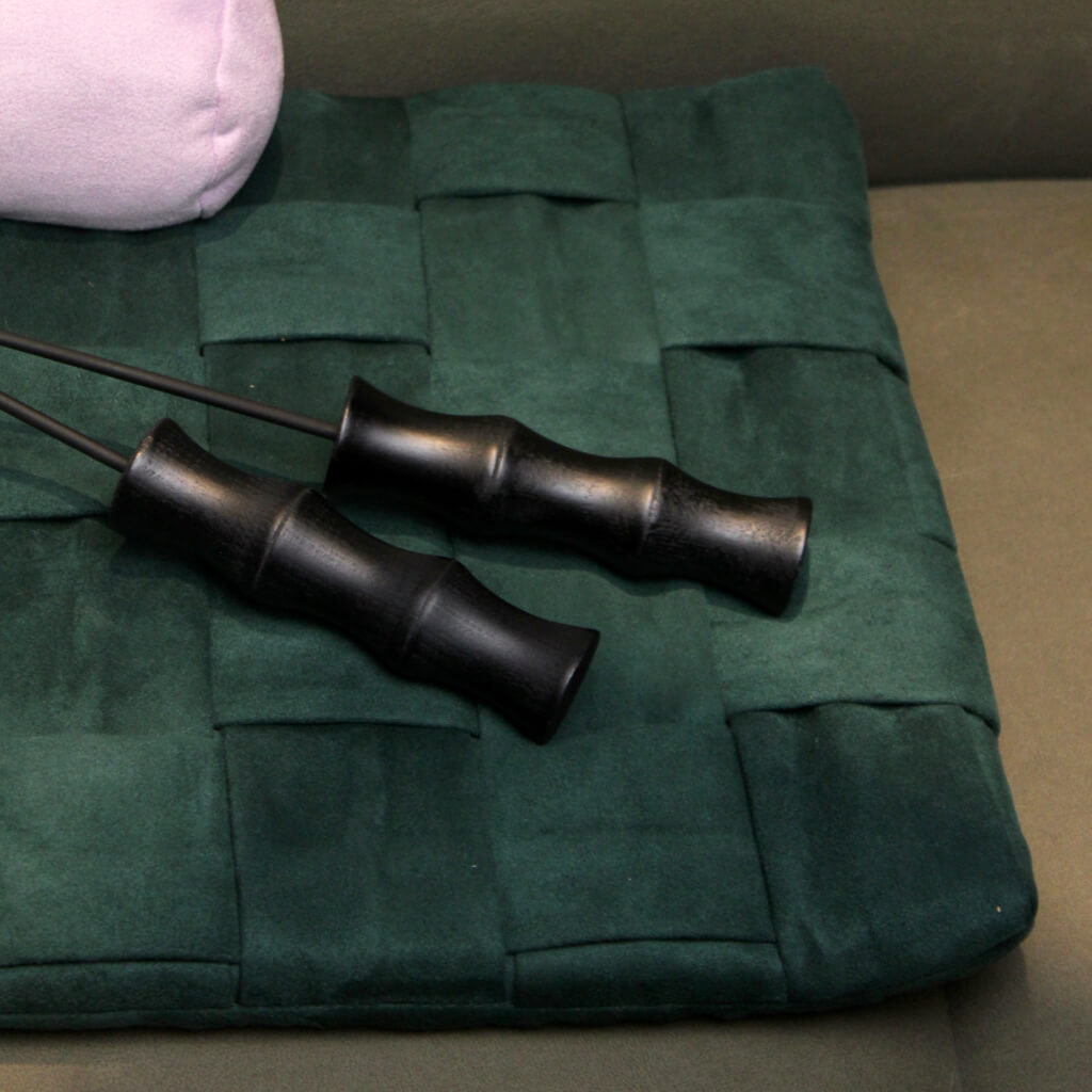 Close-up of bamboo-handled cat teasers lying on a dark green mat. The sleek black bamboo handle highlights the premium design.