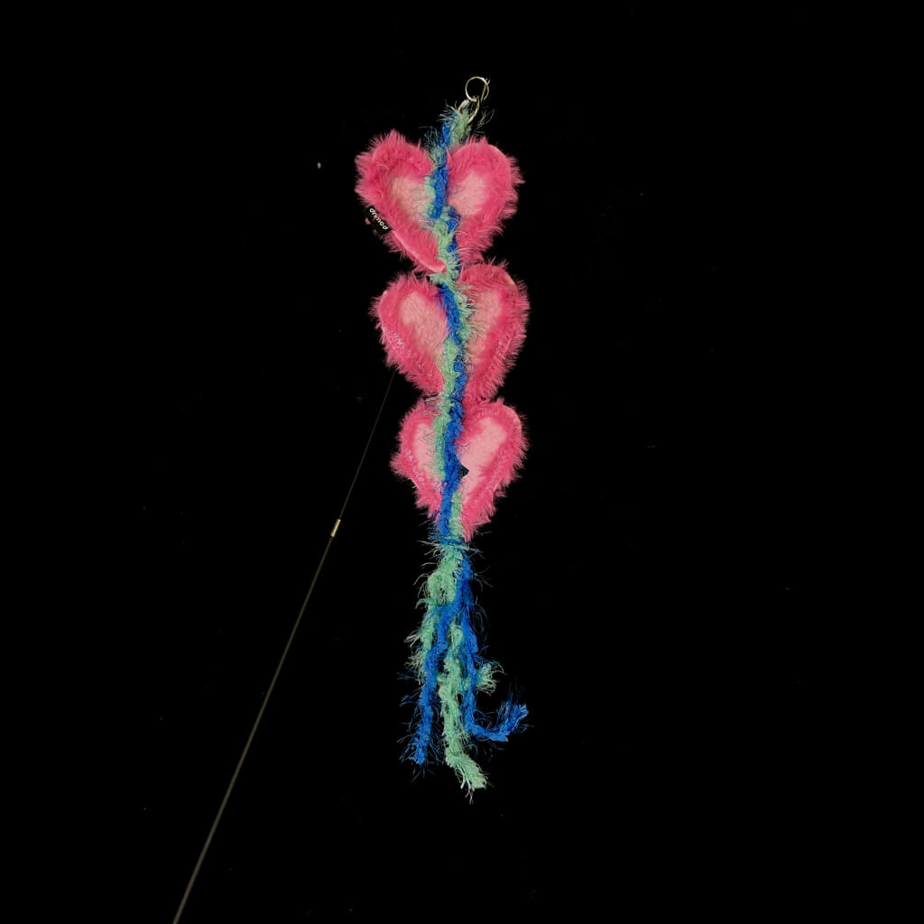 A pink heart-shaped attachment hanging from the bamboo cat teaser, set against a dark backdrop, ready for playful interaction with your feline.