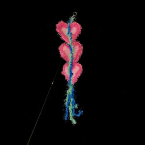A pink heart-shaped attachment hanging from the bamboo cat teaser, set against a dark backdrop, ready for playful interaction with your feline.
