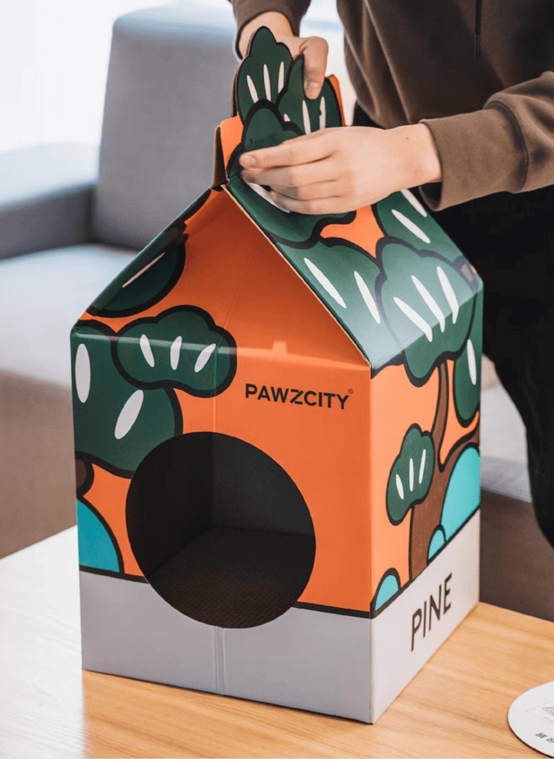 Hands assembling the Pine-themed Bonsai MilkBox Cat House, featuring Japanese bonsai tree illustrations.